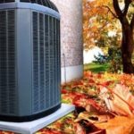 Air conditioning unit beside building, surrounded by autumn leaves, highlighting HVAC services by Hancock & Son Plumbing.