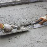 Human hands in gloves smoothing wet concrete for a construction project related to Hancock & Son plumbing services.