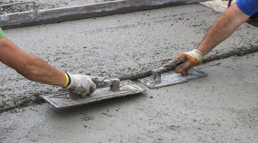 Two workers using concrete trowels on freshly poured concrete for Hancock & Son Plumbing services in home maintenance.