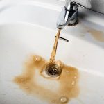 Faucet with brown water pouring into a stained white sink showing plumbing issues related to water safety.
