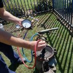 Technician using a pressure gauge outdoors to ensure safe drinking water during backflow testing for Hancock & Son Plumbing.