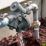 Water meter and pipes showing flowing water and rusty fittings, relating to backflow testing by Hancock & Son Plumbing.