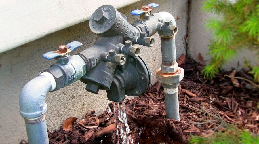 Water valve assembly in garden with blue handles, pipes, and flowing water for irrigation by Hancock & Son Plumbing.