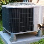 Air conditioning unit on concrete blocks amidst greenery, showcasing Hancock & Son's summer maintenance services.