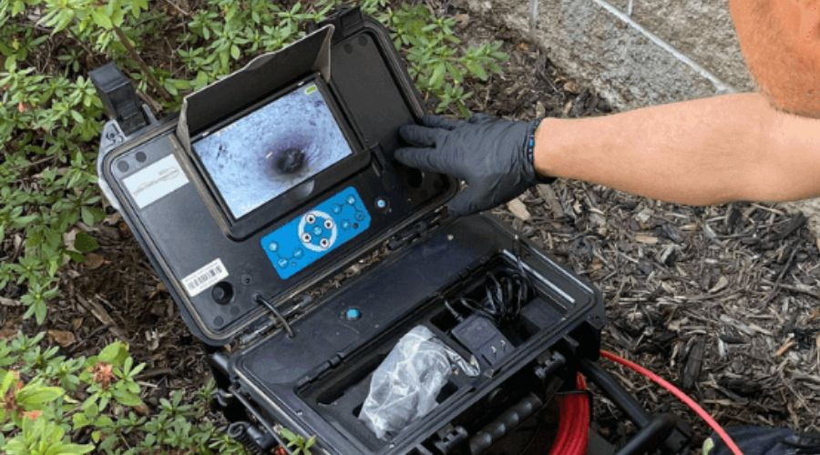 Technician in gloves inspecting HVAC control panel, monitor display showing equipment data among surrounding greenery.