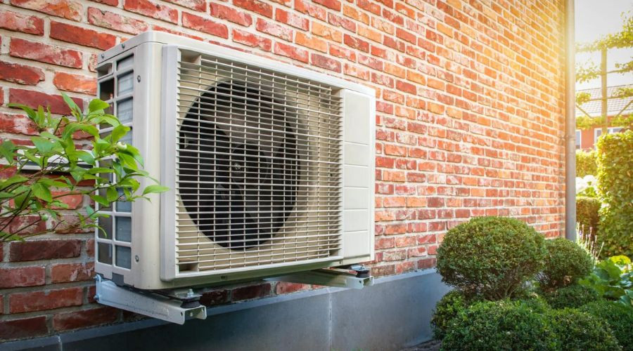 Air conditioning unit on a brick wall with green foliage and trimmed bushes, showcasing efficient HVAC solutions.