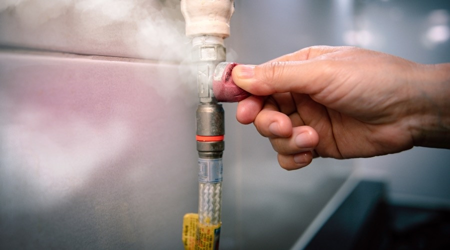 Hand adjusting a valve on a plumbing pipe, with steam visible, illustrating safety measures for recognizing gas leaks in home plumbing systems.